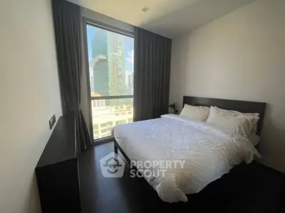 Modern bedroom with large window offering city view, featuring a cozy bed and sleek furnishings.