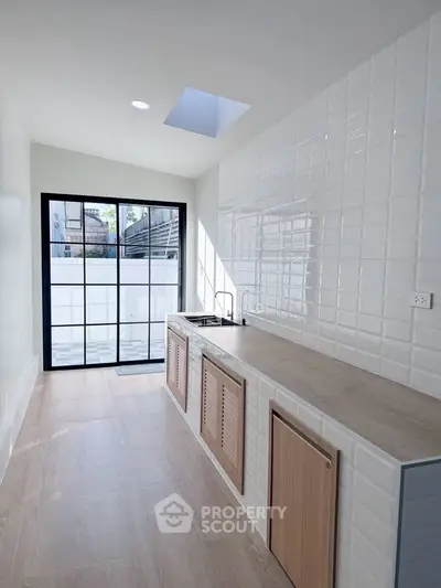 Modern kitchen with sleek design, featuring a skylight and large window for natural light.