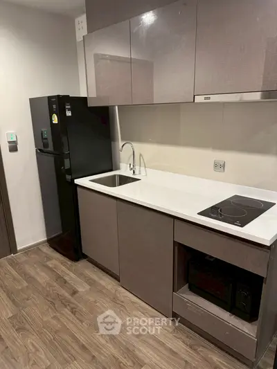 Modern kitchen with sleek cabinets, electric stove, and black refrigerator on wooden flooring.