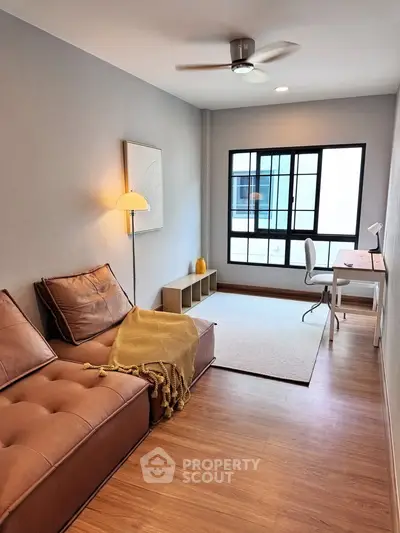 Modern living room with cozy leather sofa and study area, featuring large window and stylish decor.