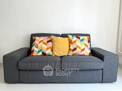Stylish gray sofa with colorful chevron pillows in modern living room.