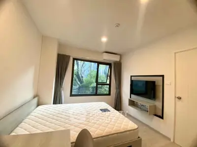 Modern bedroom with large window and wall-mounted TV, featuring a comfortable bed and minimalist decor.