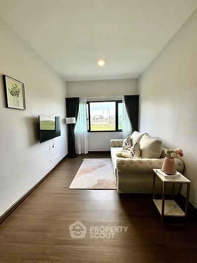 Cozy living room with elegant sofa and wall-mounted TV, featuring a large window for natural light.