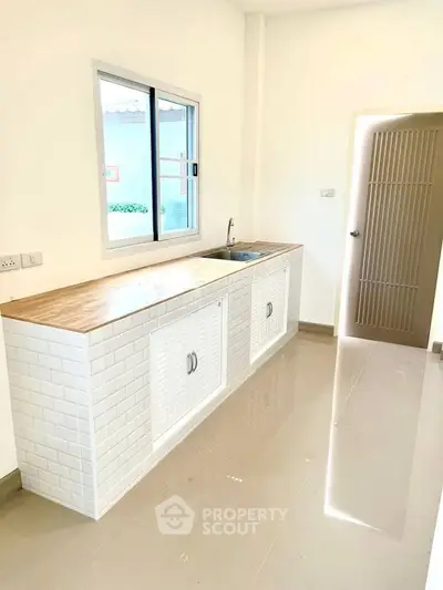Modern kitchen with sleek white cabinetry and wooden countertop, featuring a large window for natural light.