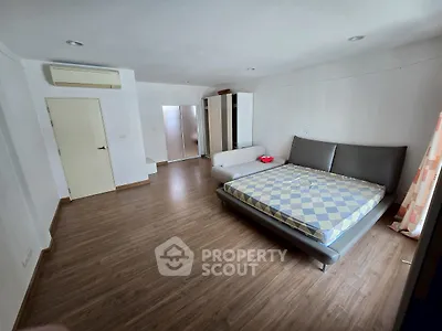 Spacious bedroom with modern furnishings and wooden flooring in a well-lit apartment.