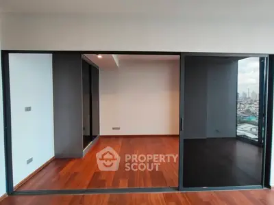 Spacious room with wooden flooring and large sliding glass doors offering city views.