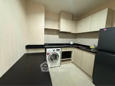 Modern kitchen with sleek cabinetry, washing machine, and black countertops in a contemporary apartment.