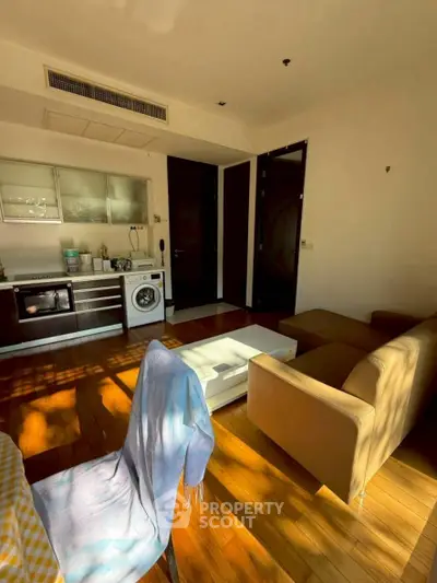 Modern living room with integrated kitchen and washing machine, featuring wooden flooring and cozy seating.