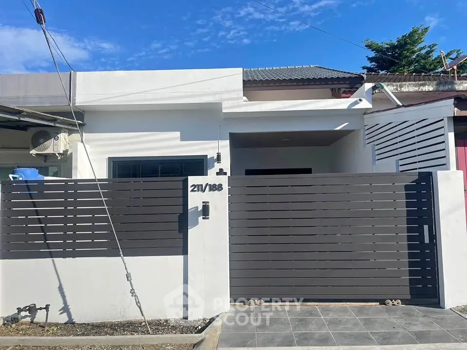 Modern single-story house with sleek fence and tiled driveway under clear blue sky.