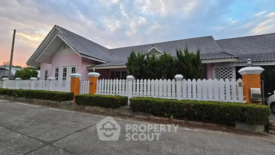 Charming pink house with white picket fence and lush greenery, perfect suburban living.