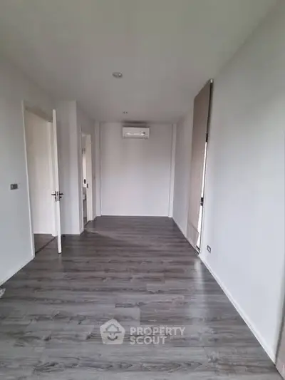 Spacious empty room with modern flooring and air conditioning unit.