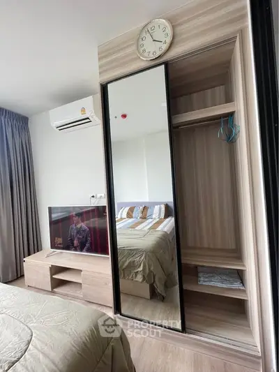 Modern bedroom with mirrored wardrobe and wall-mounted TV, featuring stylish decor and natural light.