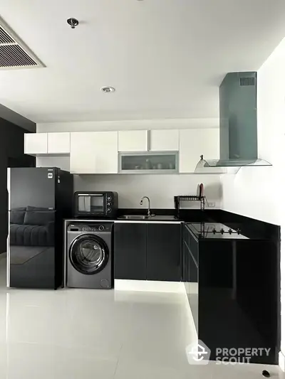 Modern kitchen with sleek black and white cabinetry, featuring a washing machine and appliances.