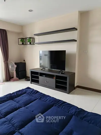 Modern bedroom with sleek TV stand and floating shelves, featuring a cozy blue comforter and natural light.