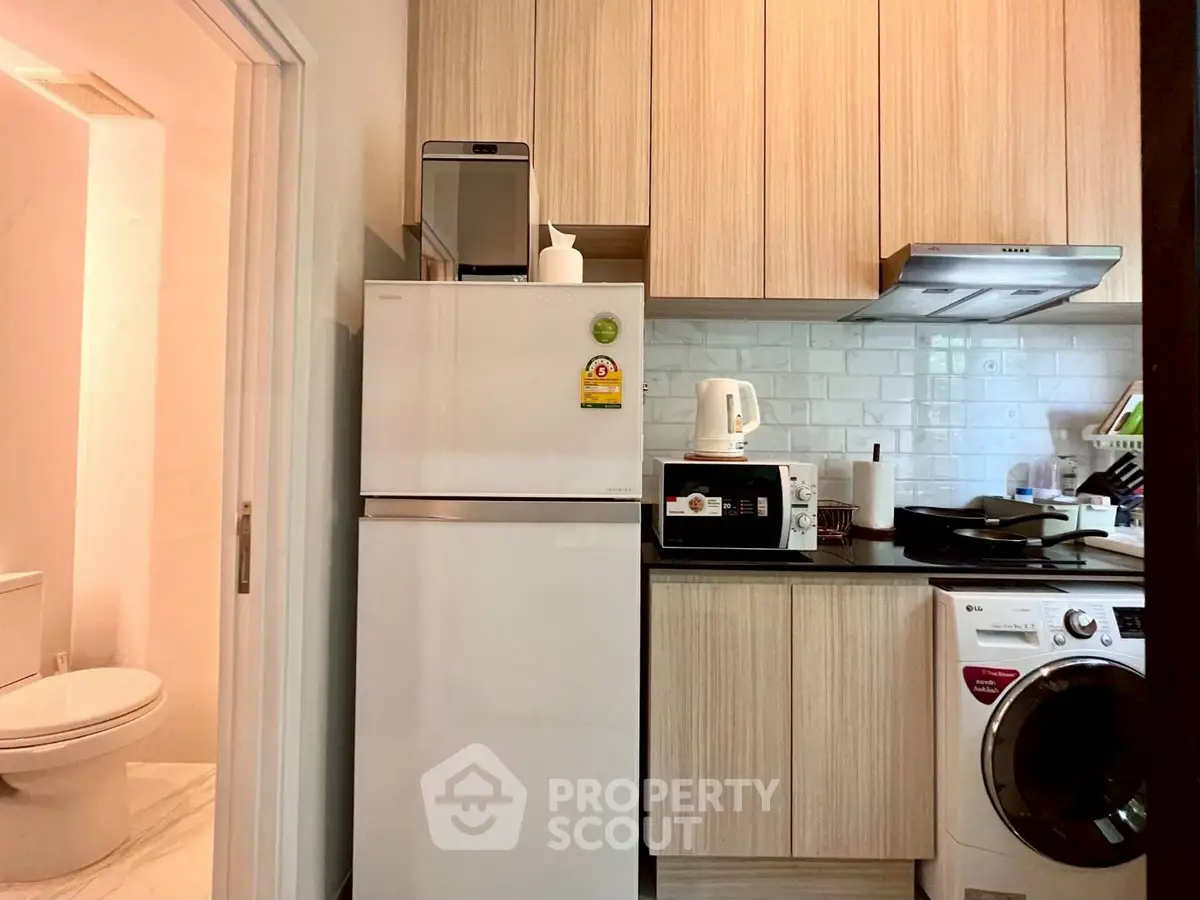 Modern compact kitchen with wooden cabinets, appliances, and adjacent bathroom.