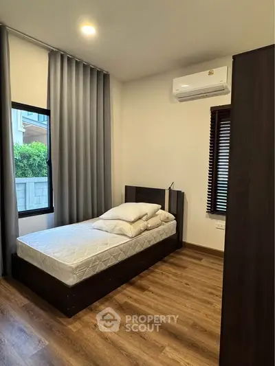 Cozy bedroom with single bed, wooden flooring, and air conditioning in modern apartment.