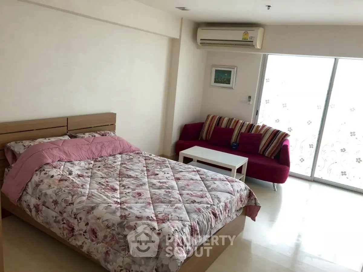 Spacious bedroom with floral bedding and cozy seating area near balcony.