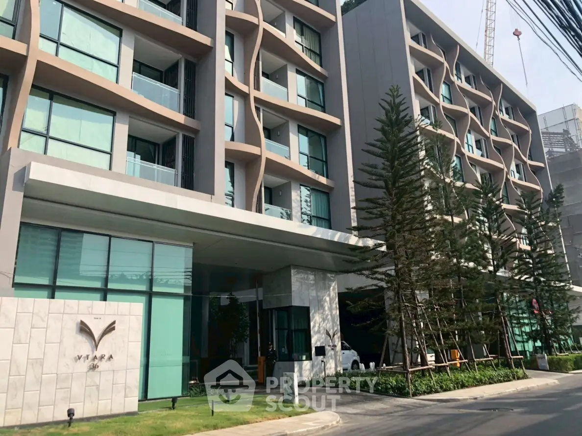 Modern apartment building with sleek design and lush landscaping, featuring large windows and balconies.
