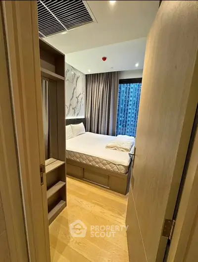 Cozy bedroom with modern decor and city view, featuring wooden flooring and elegant curtains.