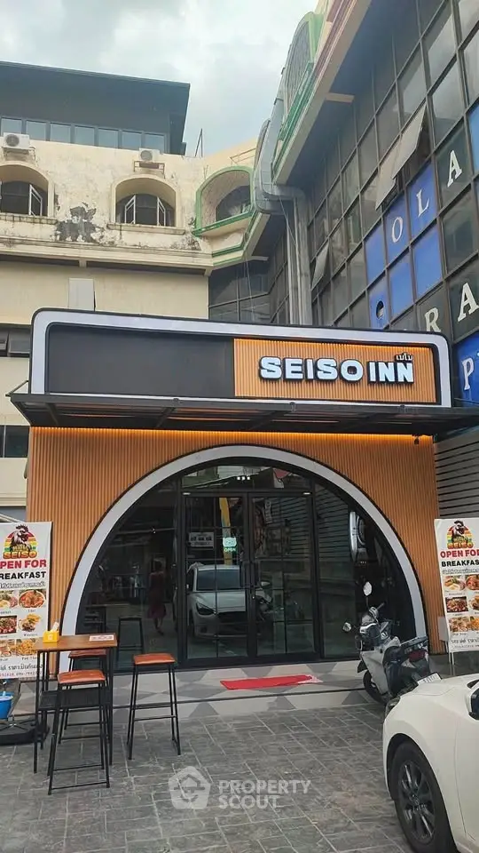Modern restaurant entrance with stylish signage and outdoor seating in urban setting.