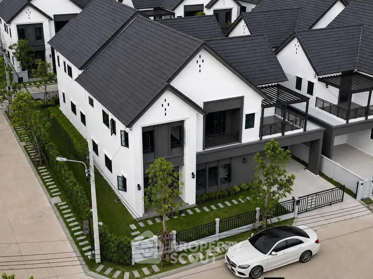 Modern white townhouse with sleek design and black roof, featuring a spacious driveway and lush greenery.