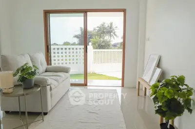 Bright living room with sliding glass doors opening to a lush garden view, featuring cozy seating and modern decor.