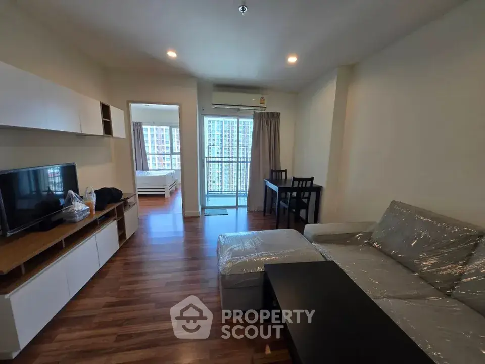 Modern living room with cozy sofa and TV, open layout leading to bedroom and balcony with city view.