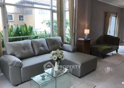 Spacious living room with modern gray sofa and large windows overlooking greenery.