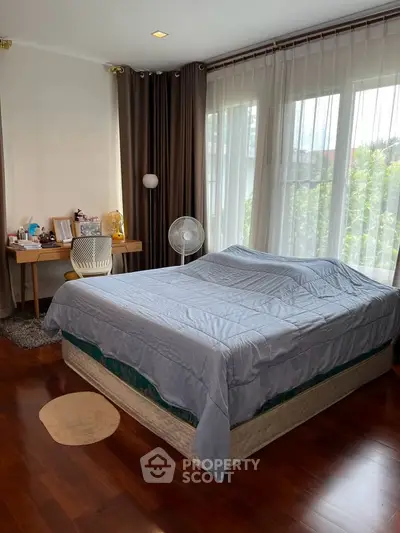 Spacious bedroom with large windows and elegant decor, featuring a cozy bed and stylish workspace.