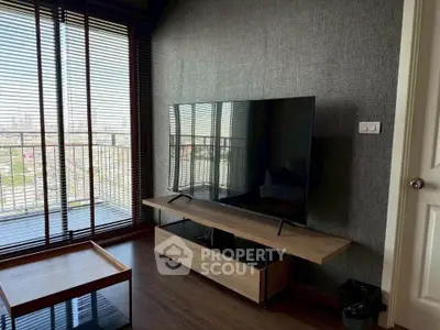 Modern living room with large TV and city view from balcony, featuring sleek wooden furniture and stylish decor.