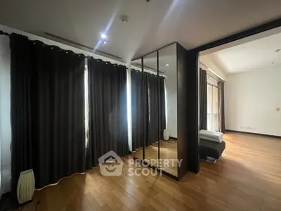 Spacious bedroom with mirrored wardrobe and wooden flooring, featuring large windows with dark curtains.