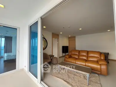 Spacious modern living room with leather sofa and large glass doors opening to a balcony with a view.
