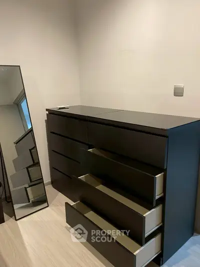 Modern bedroom with sleek black dresser and full-length mirror, showcasing minimalist design.