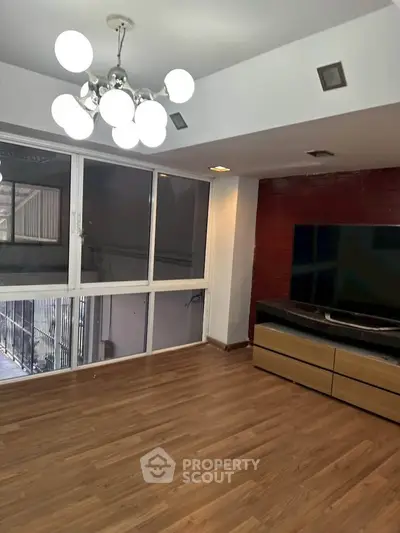 Spacious living room with modern lighting and large TV, featuring wood flooring and ample natural light.
