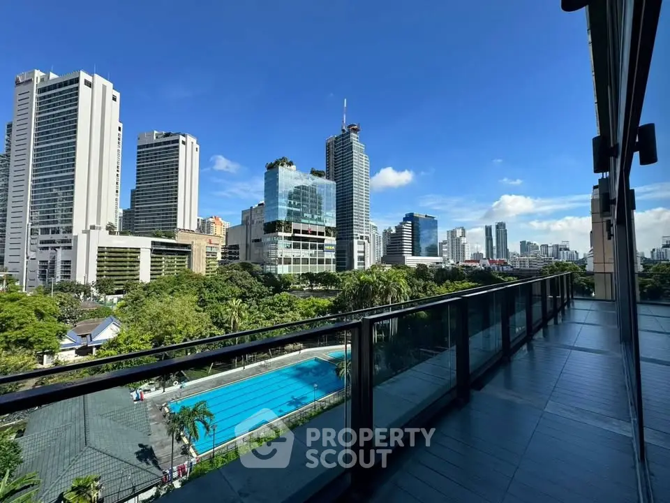 Stunning cityscape view from a modern balcony overlooking a pool and lush greenery.