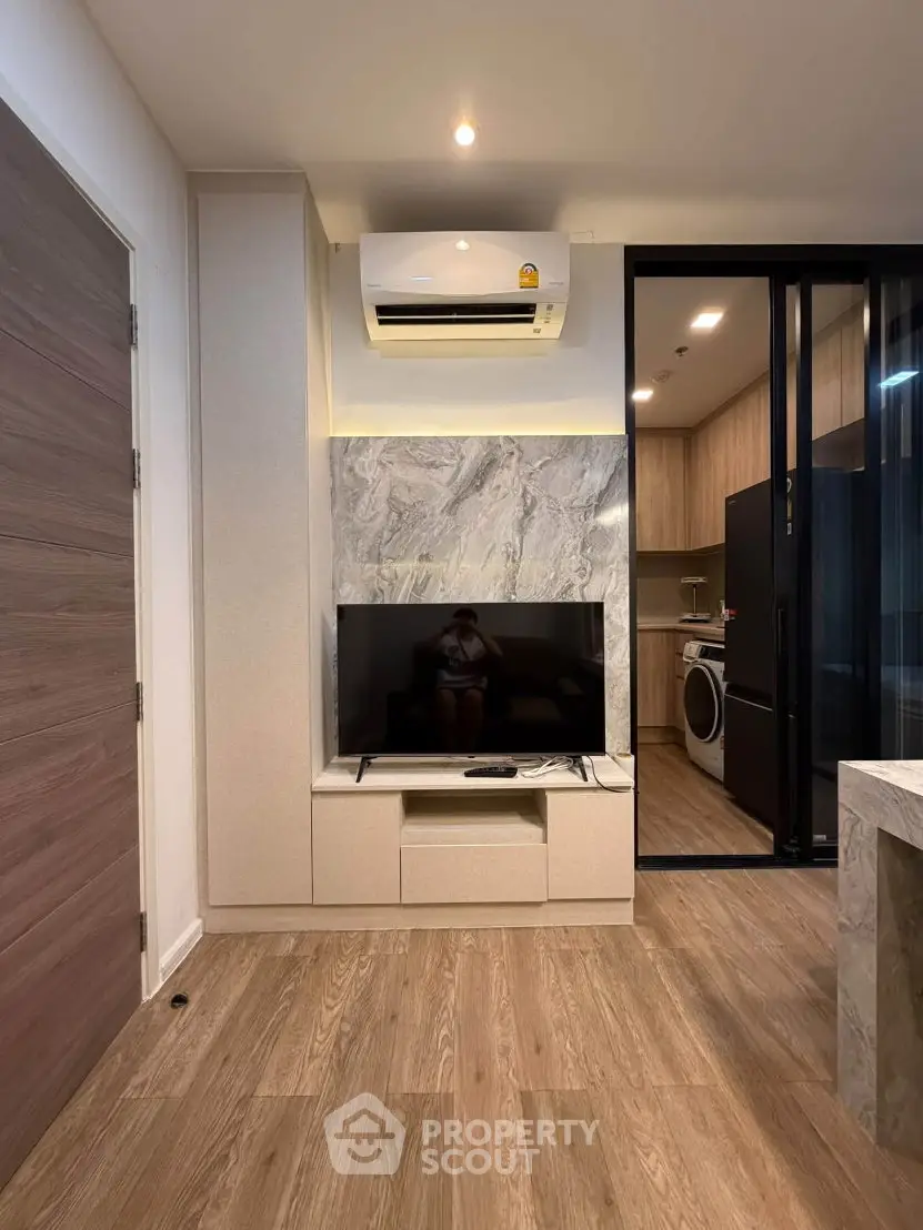 Modern living room with TV, air conditioning, and view into a sleek kitchen with appliances.