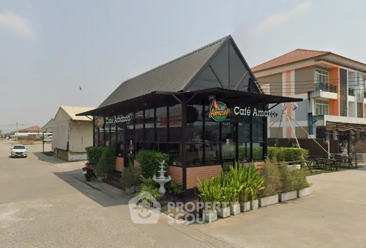 Charming café with modern glass exterior and lush greenery, perfect for a relaxing coffee break.