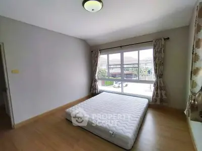 Spacious bedroom with large window and natural light, featuring a minimalist design and wooden flooring.