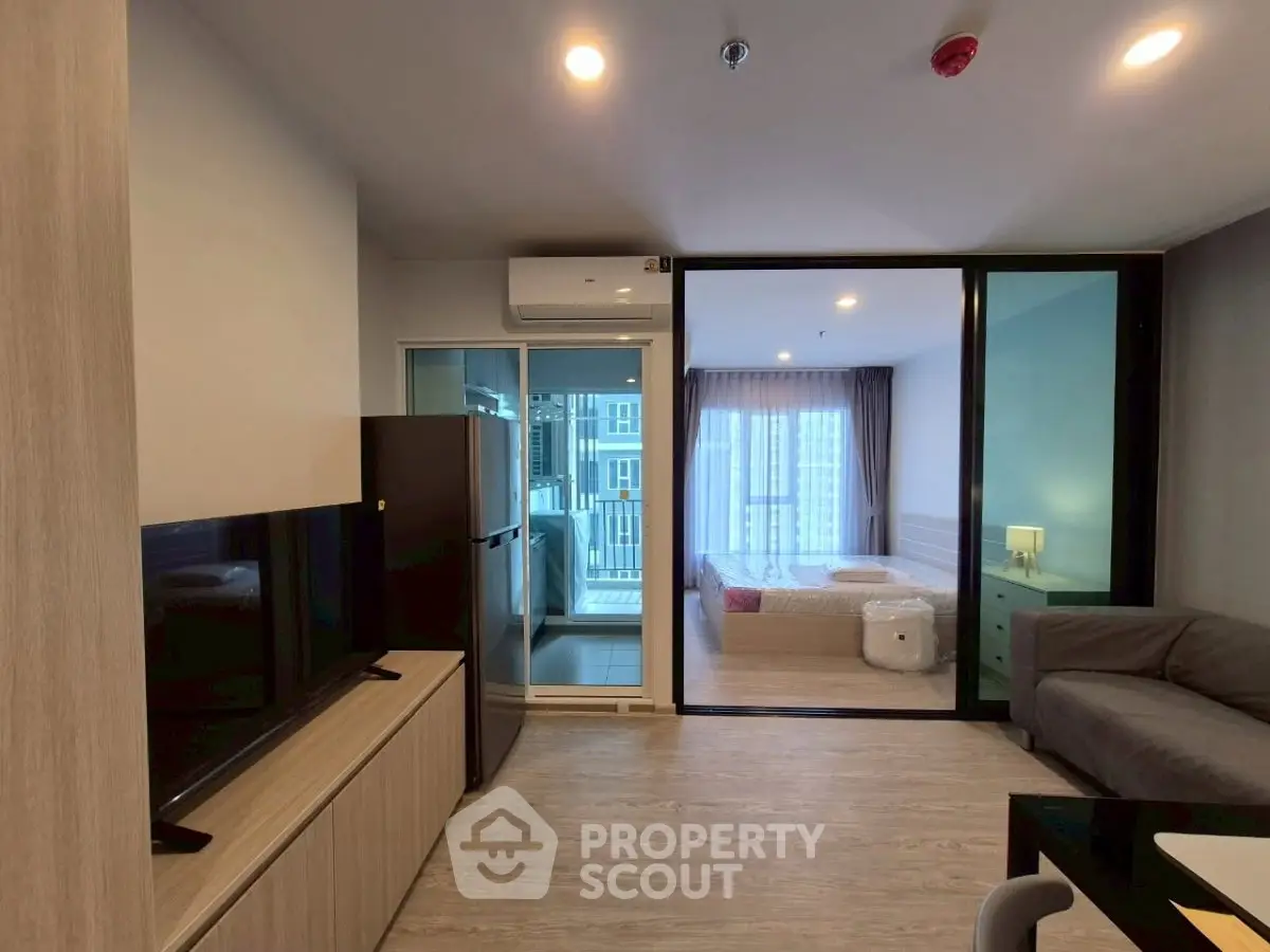 Modern apartment interior with open living room and bedroom, featuring sleek furniture and large windows.