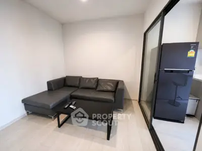 Modern living room with sleek black sofa and glass sliding door leading to kitchen area.