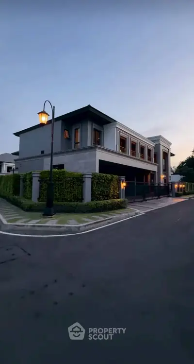 Elegant modern house exterior with lush greenery and street lamp at dusk.