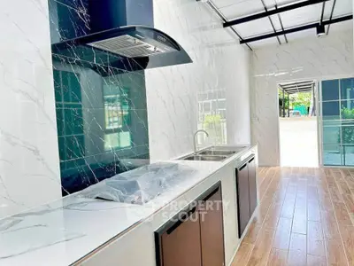 Modern kitchen with sleek design and ample natural light, featuring marble countertops and wooden flooring.