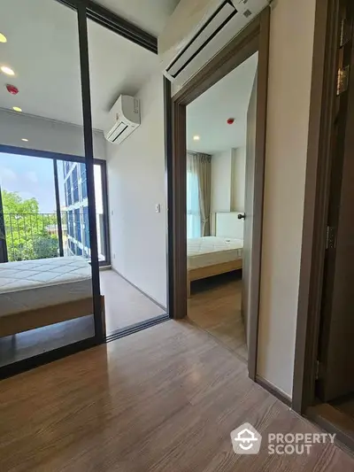 Modern apartment interior with two bedrooms and air conditioning, featuring large windows and wooden flooring.