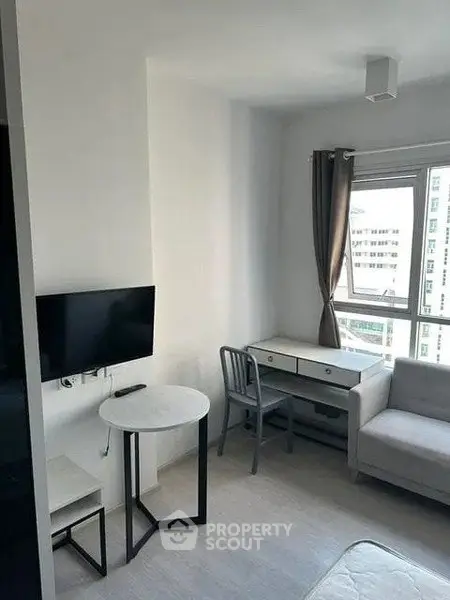 Modern living room with sleek furniture and large window offering city views.