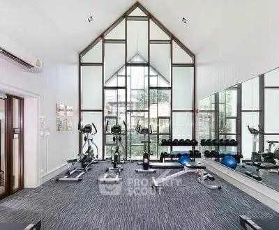 Modern gym with large windows and fitness equipment in a stylish building.