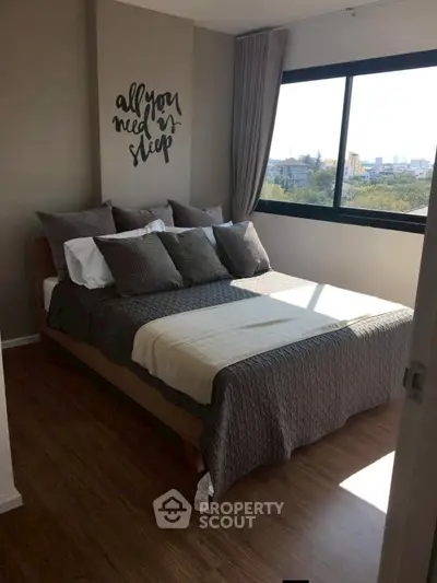 Cozy bedroom with stylish decor and large window offering natural light and city view.