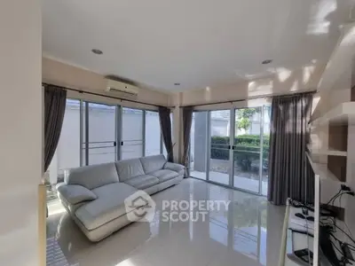 Spacious living room with modern white sofa and large windows offering garden view.