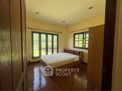 Cozy bedroom with large windows and wooden flooring, offering serene garden views.