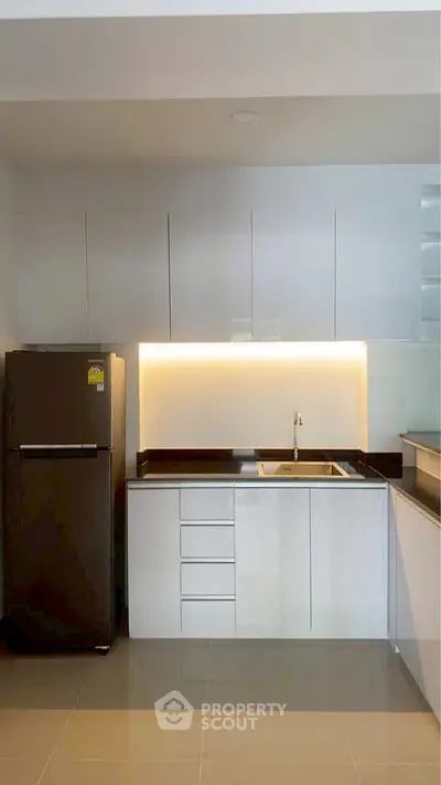 Modern kitchen with sleek cabinetry and built-in lighting, featuring a stainless steel fridge and elegant design.