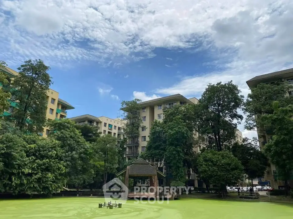 Scenic view of modern residential buildings surrounded by lush greenery and a tranquil pond.